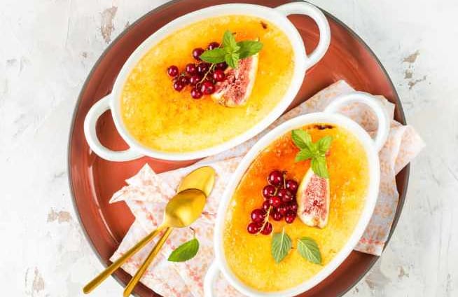 Brown plate containing two creme brulee with mint leaves, berries and passion fruit on top