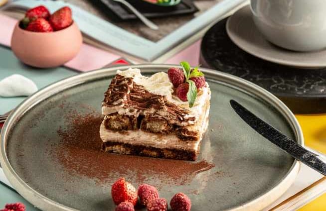 Square slice of Tiramisu, powder chocolate and berries on the side